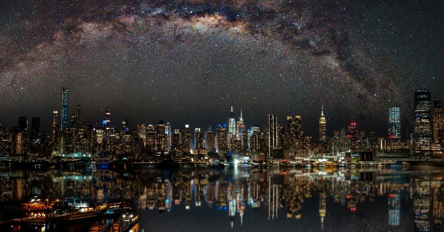 A night-time view of the cityscape with stars decorating the sky and reflections in a large body of water